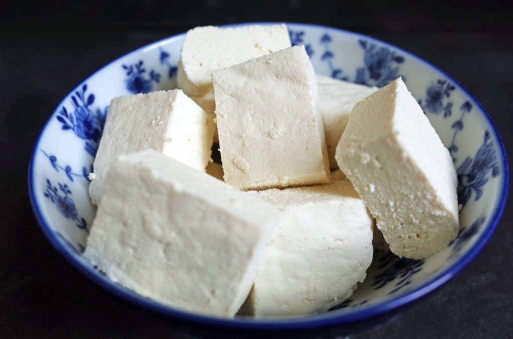 Homemade firm tofu made from soy milk cut into pieces and in a Chinese white and blue bowl