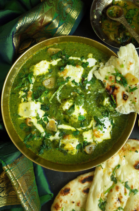 Palak Paneer in a gold bowl topped with cream and coriander with Garlic and Coriander Naan bread on the side