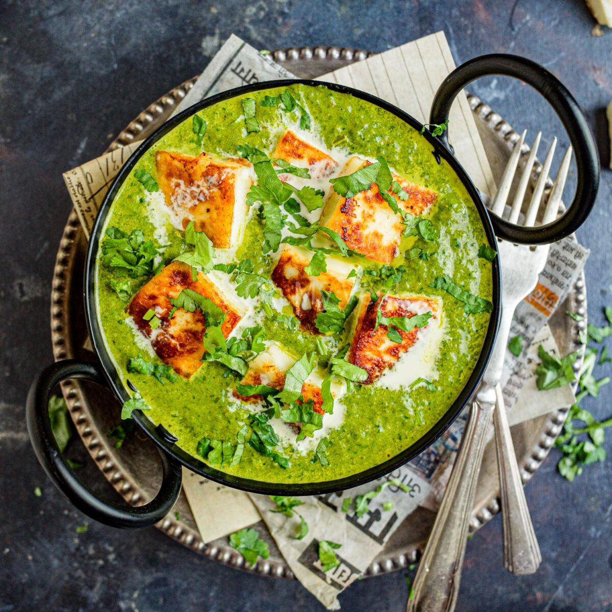 Palak paneer in a black kadai with cutlery on the side.