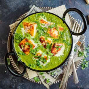 Palak paneer in a black kadai with cutlery on the side.