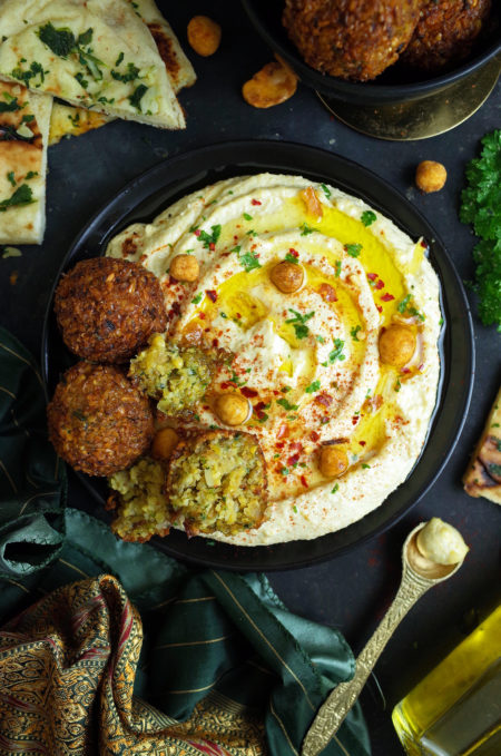 Plain Hummus topped with olive oil, parsley, roasted chickpeas, paprika and falafels on a black plate with garlic and coriander naan bread