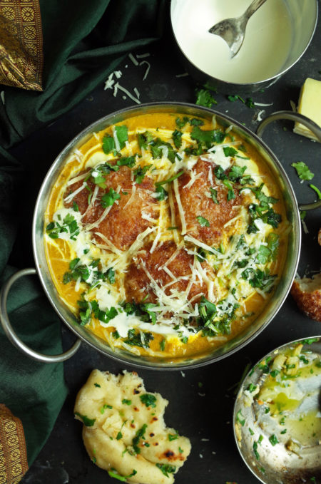 Malai Kofta topped with coriander and cream in a silver bowl with Garlic and Coriander Naan bread