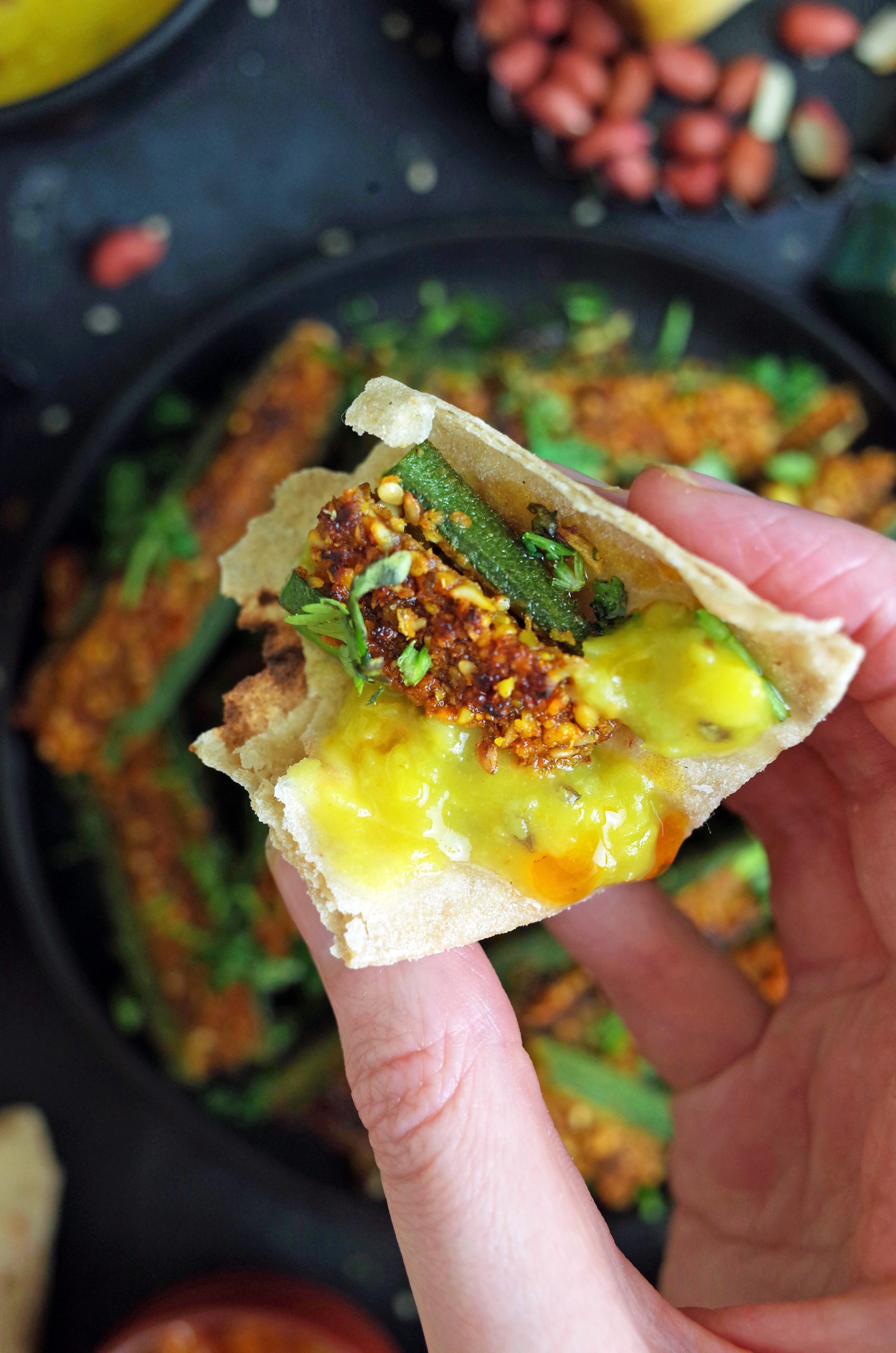 Hand holding chapati with bharli bhendi and varan. 