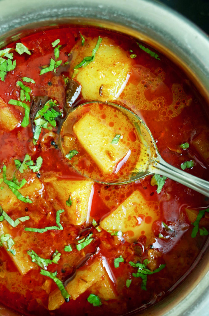 A silver spoon showing Maharashtrian Red Batata Rassa / Potato Curry topped with fresh Coriander.