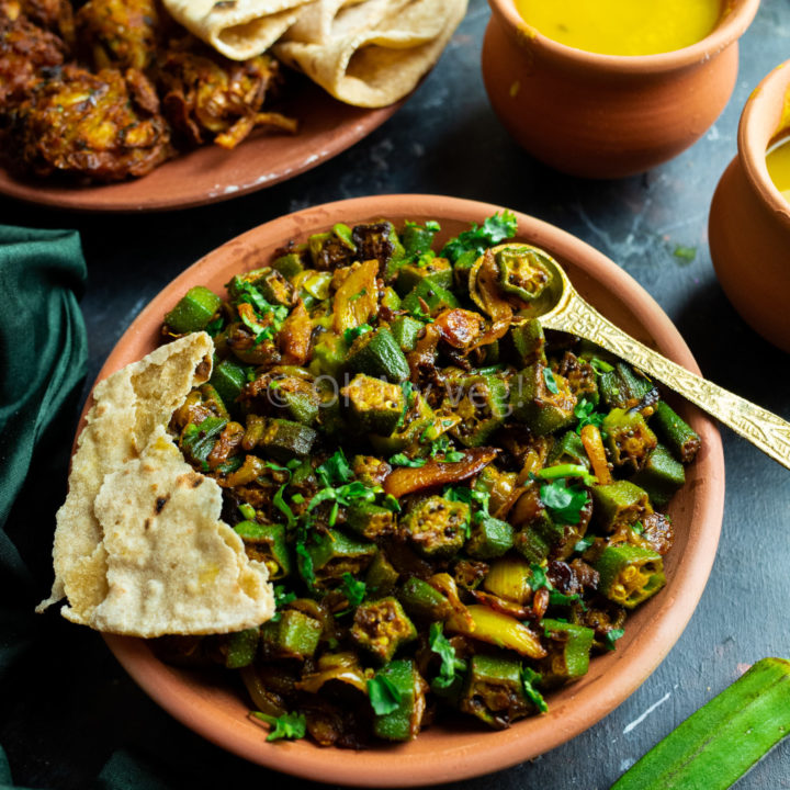 Bhindi Masala in a clay bowl, with torn chapati roti and Dal, Onion Bhaji in the background
