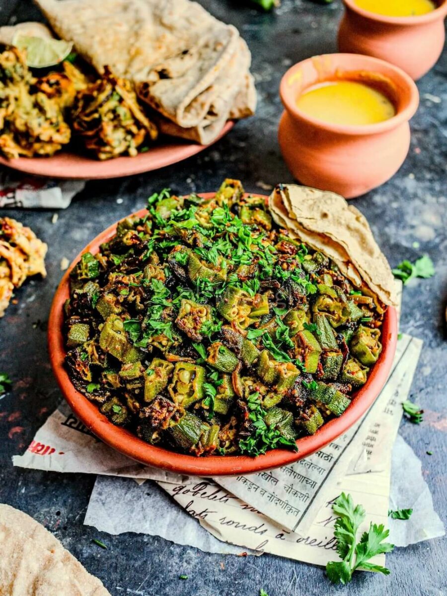 Bhindi masala okra curry in a clay bowl with dal, pakora, and roti.