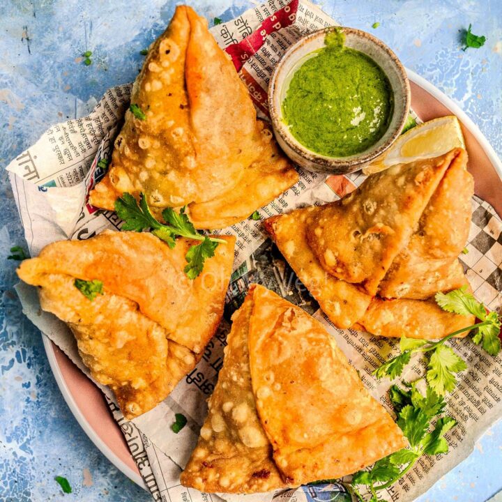 Punjabi vegetable samosa on a plate with a pot of green chutney.