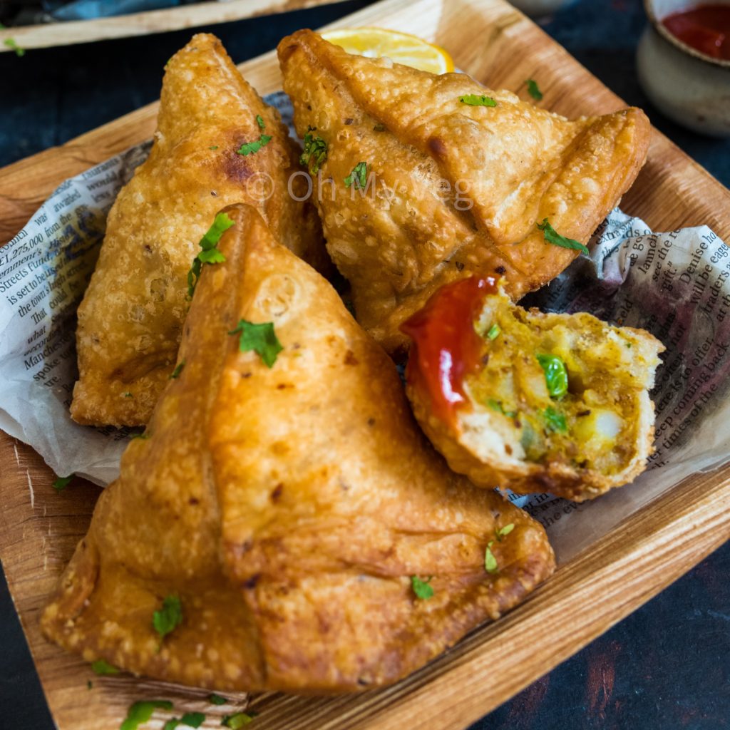 Authentic Vegetable Vegan Punjabi Samosa on a bamboo plate with one broken open dipped in ketchup
