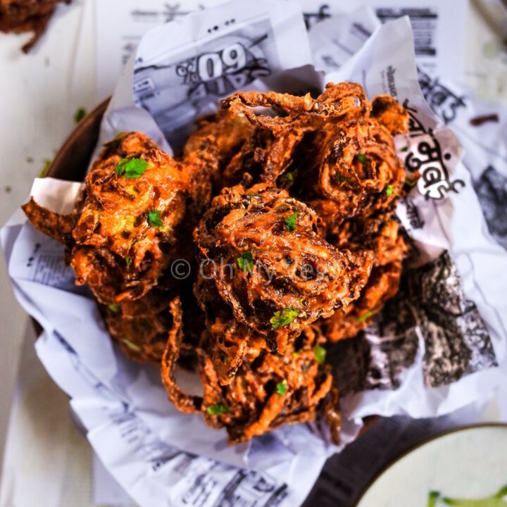 A pile of onion bhajis on newspaper with yoghurt raita on the side