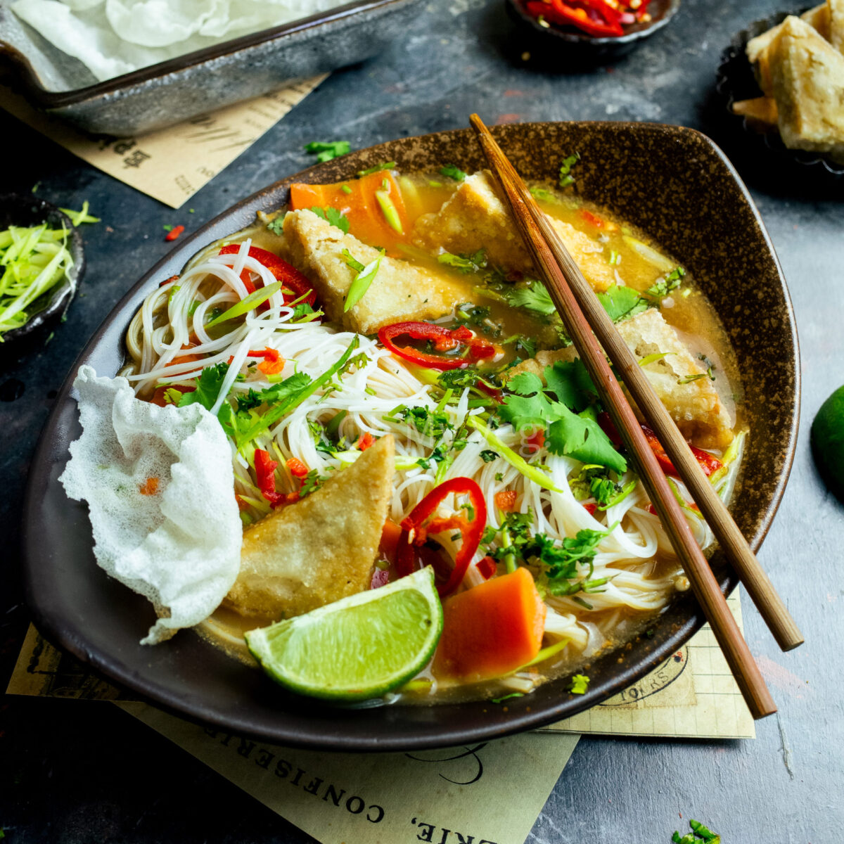 Chopsticks laying across a bowl of vegetarian tofu tum yum with vermicelli noodles