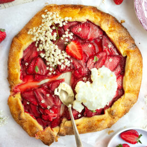 Strawberry and elderflower galette topped with whipped cream and a slice taken out