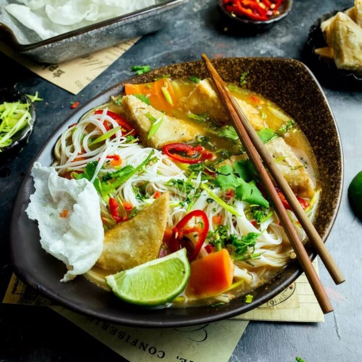 Chopsticks laying across a bowl of vegetarian tofu tum yum with vermicelli noodles