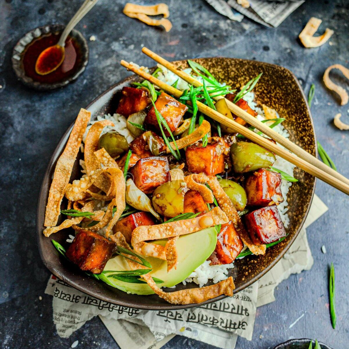 Vegan Indo-Chinese chili paneer in a bowl with rice, avocado, and wonton crisps.