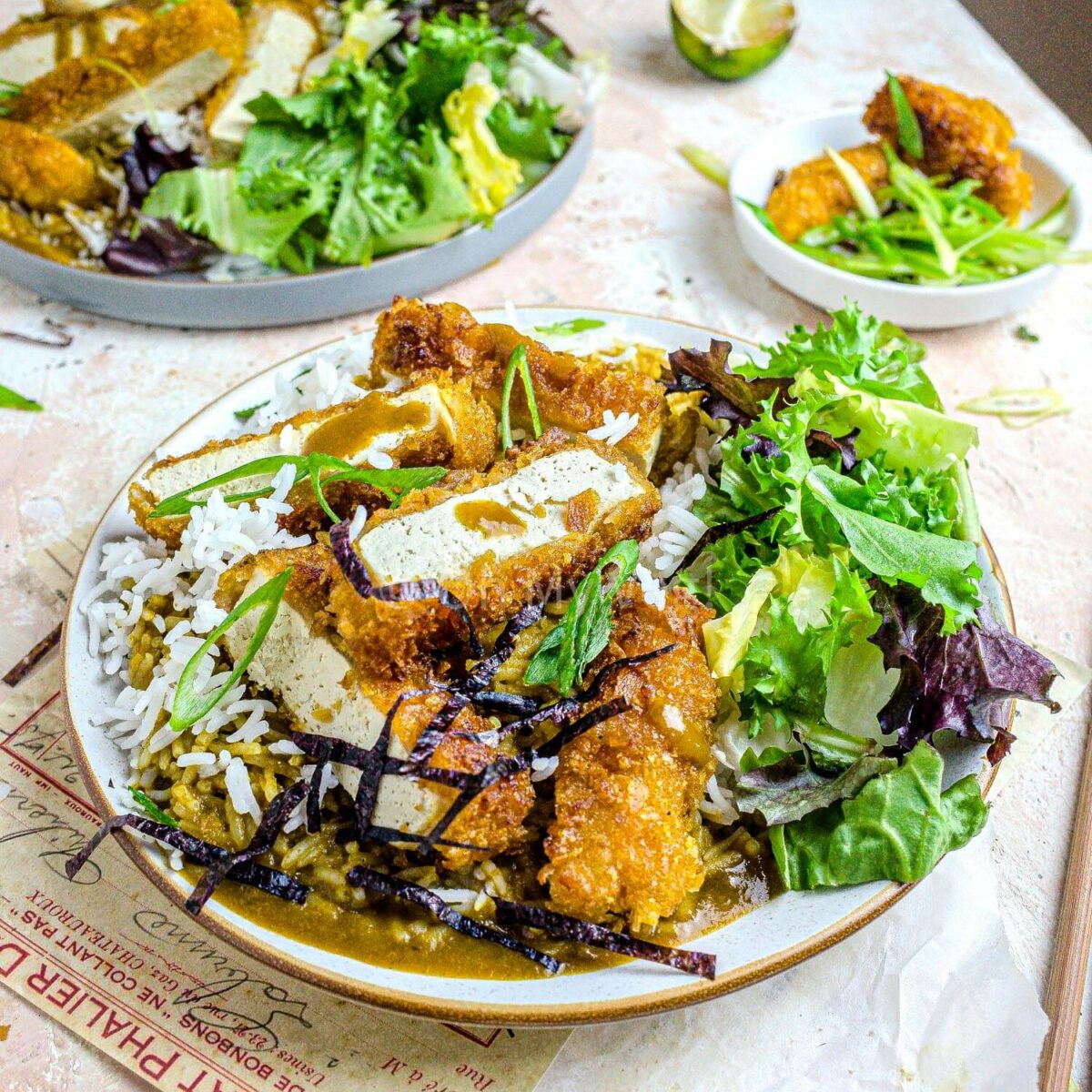 Two plates of vegan katsu curry with tofu and salad.