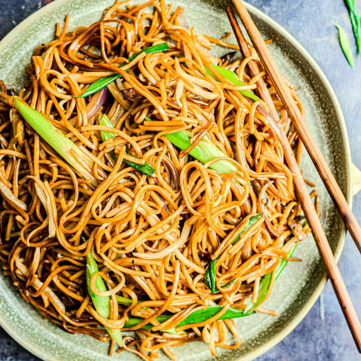 Plain chow mein noodles on a green plate with chopsticks.