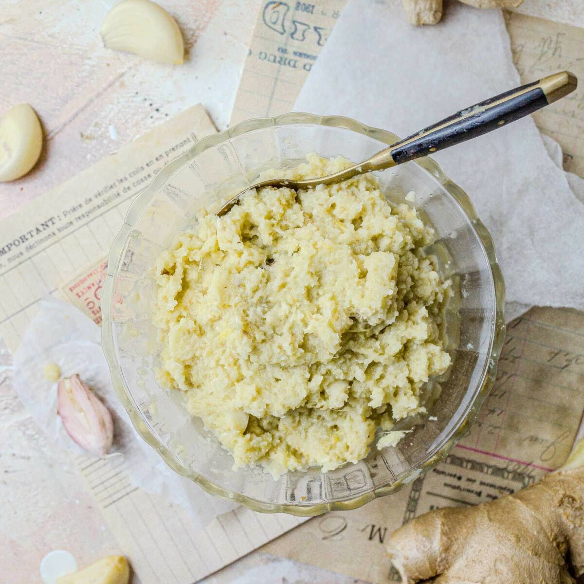 Ginger garlic paste in a glass bowl from above, with fresh ginger and garlic around it.