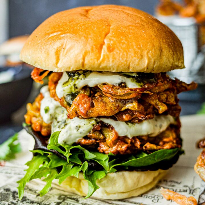 Onion bhaji burger with mint yogurt sauce and salad, on newspaper.