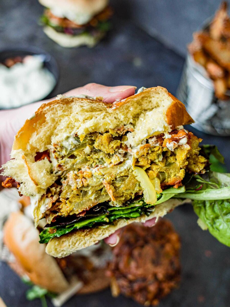 Hand holding an onion bhaji burger cut open.