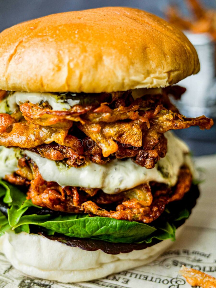 Close-up of an onion bhaji burger with yogurt sauce, chutney, and salad.