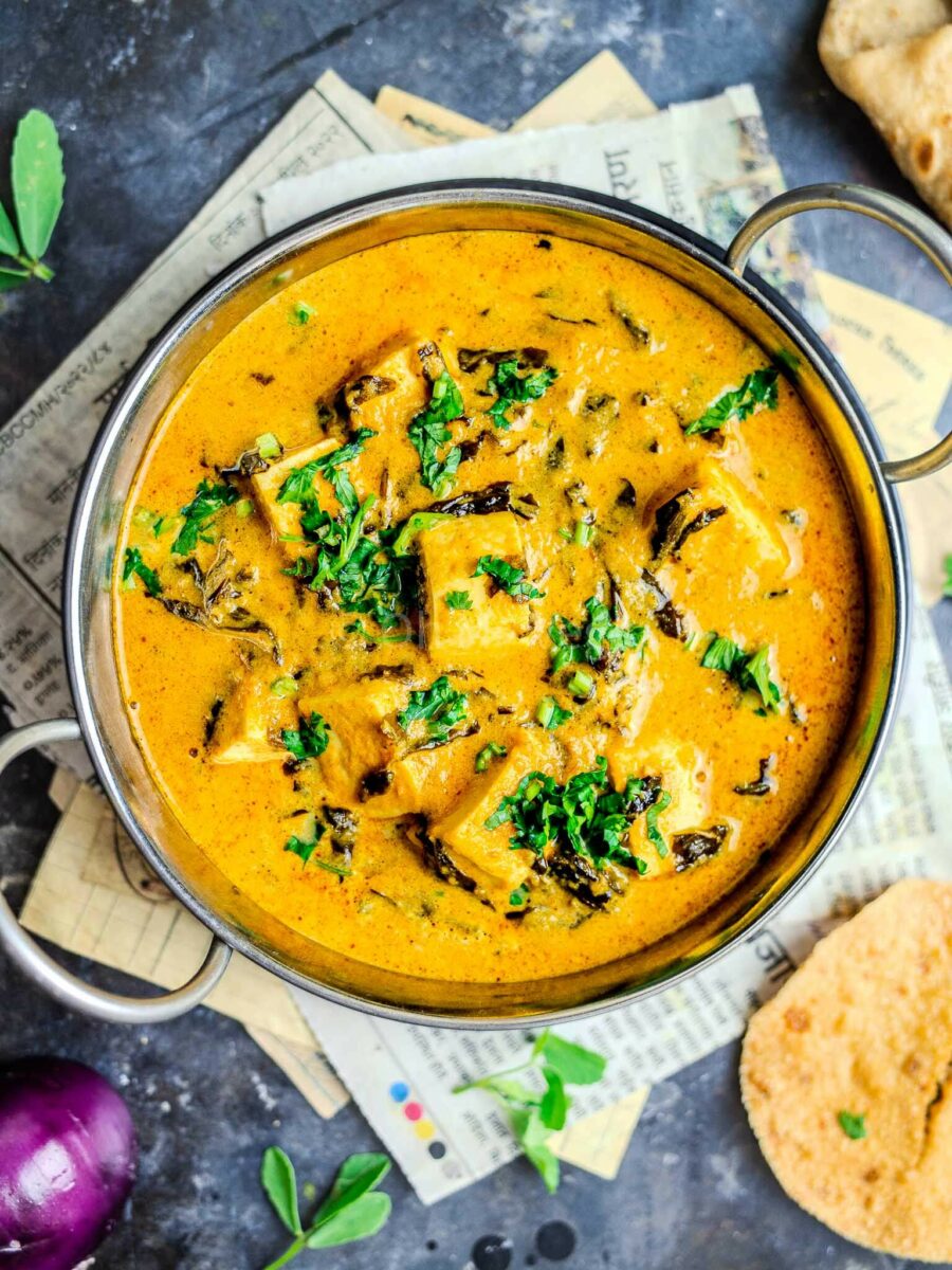 Methi malai paneer in a metal kadai, with a newspaper background. 