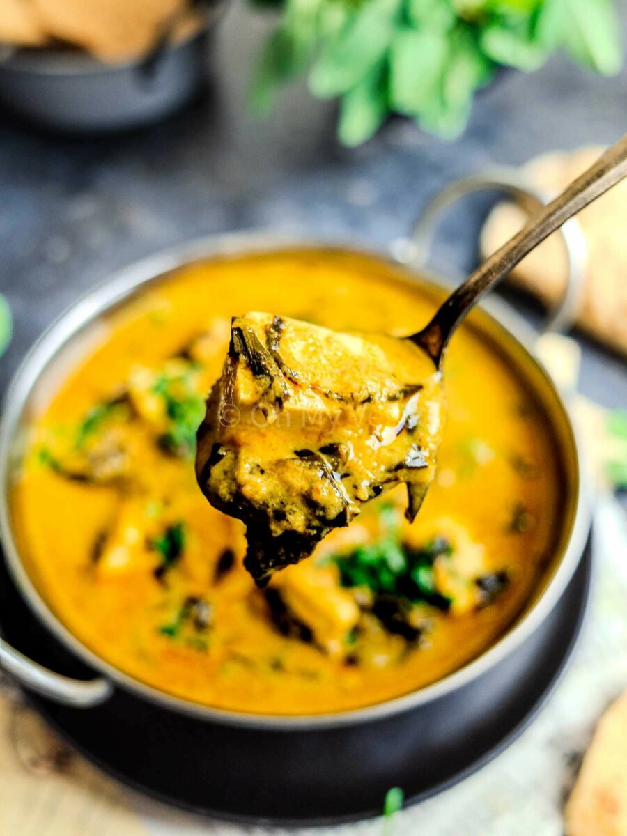 Spoon holding a piece of paneer in methi malai sauce.