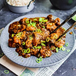 Mushroom manchurian on a plate, with chopsticks reaching for a piece.