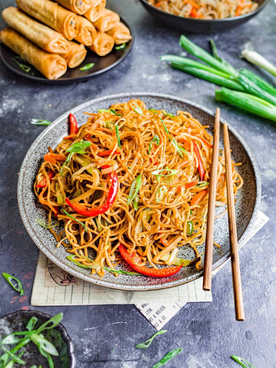 Indo Chinese veg hakka noodles with spring rolls in the background.