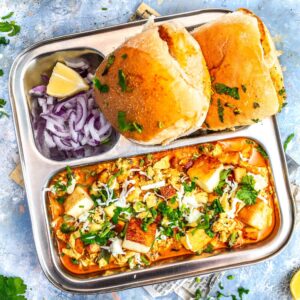 Paneer ghotala in a steel thali with pav and onion.