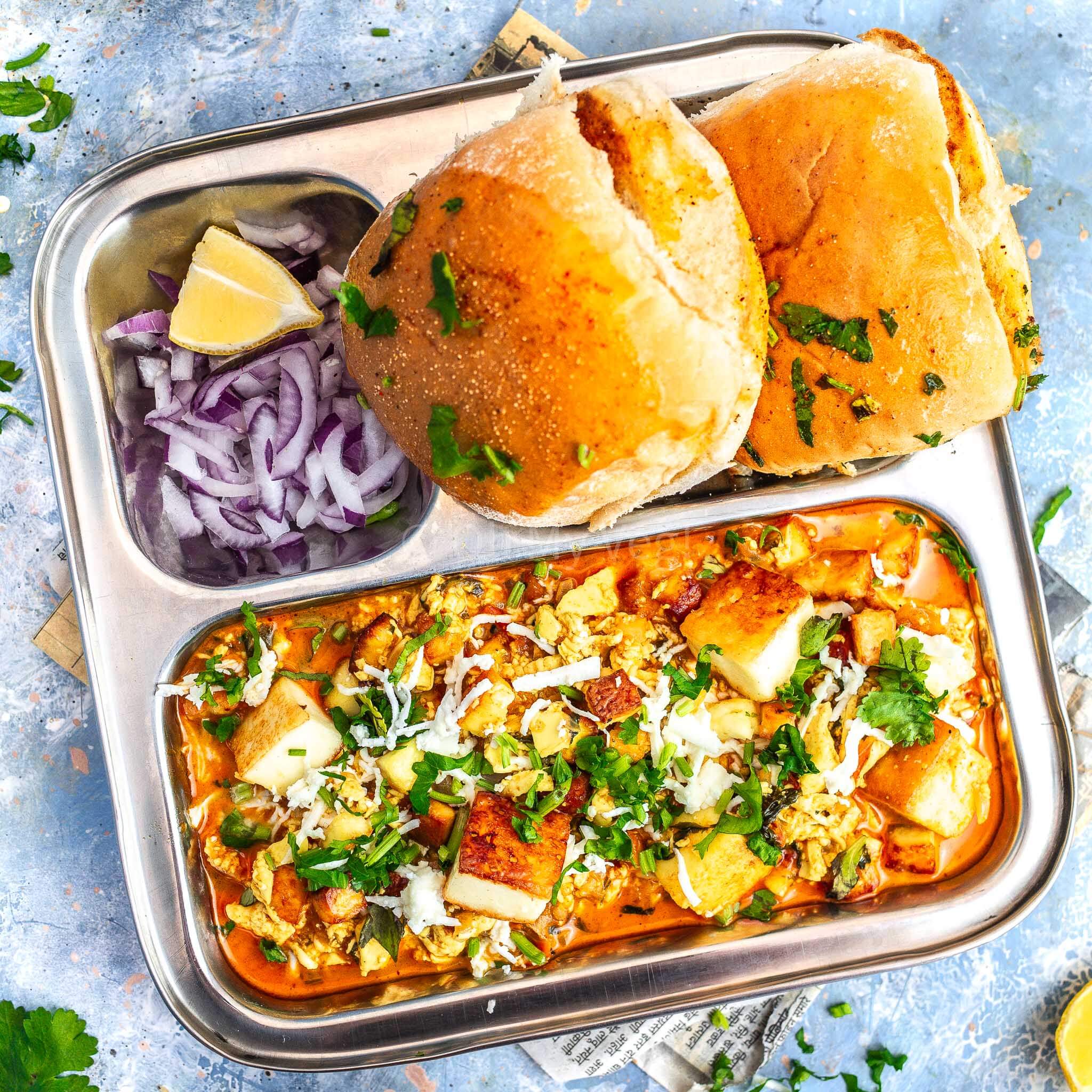 Paneer ghotala in a steel thali with pav and onion.