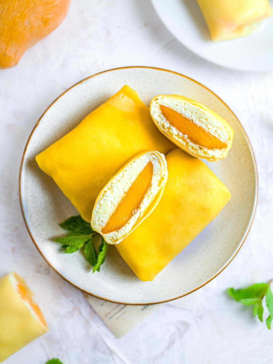 Mango pancakes Hong-Kong style on a white plate. The top one is cut in half, showing the filling.