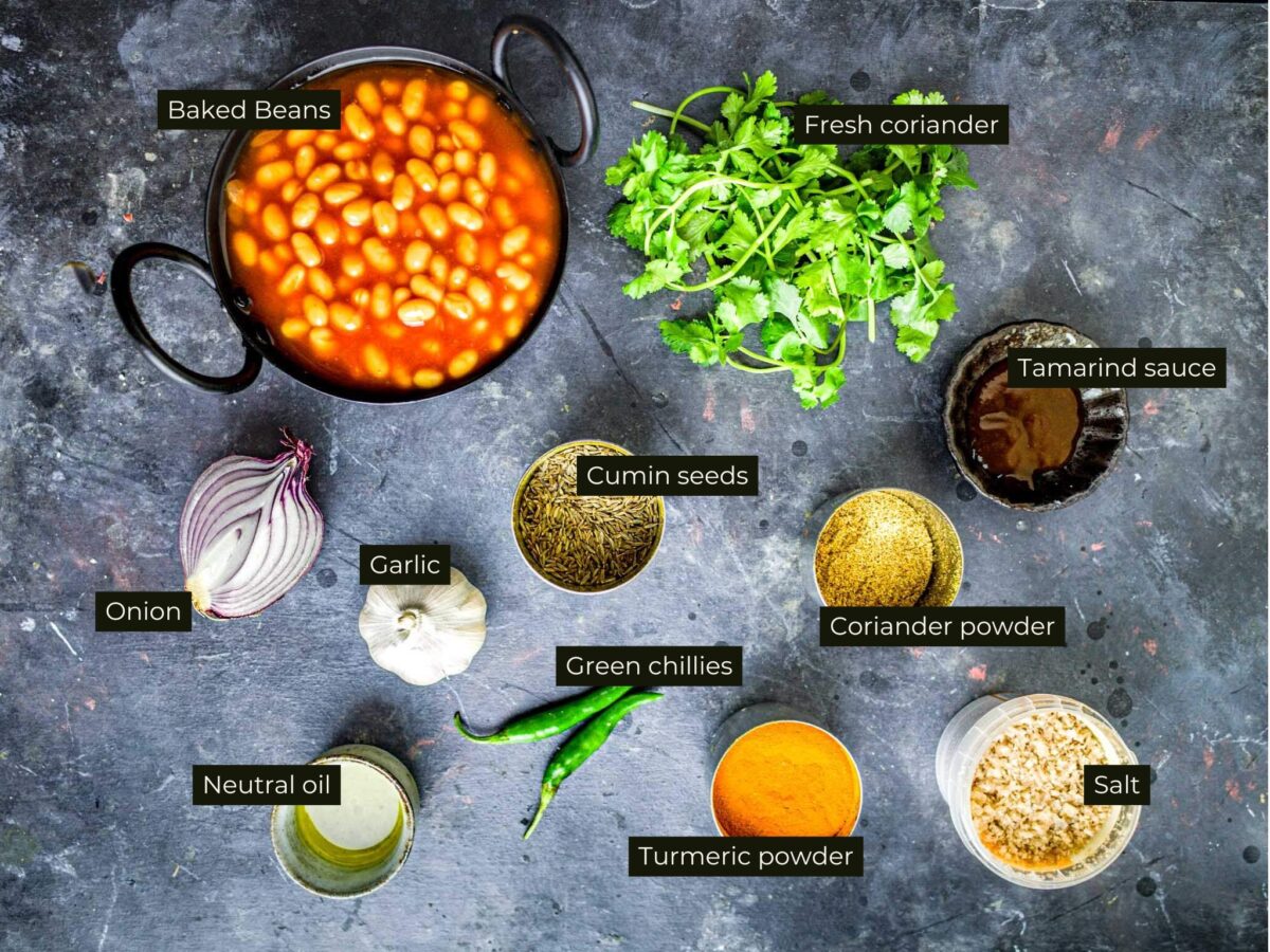 Ingredients for masala beans, labelled and laid on a black background.