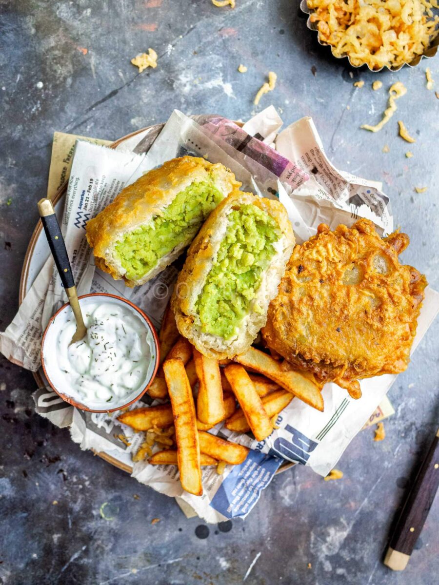 Mushy pea fritters with chips and tartare sauce, on newspaper.