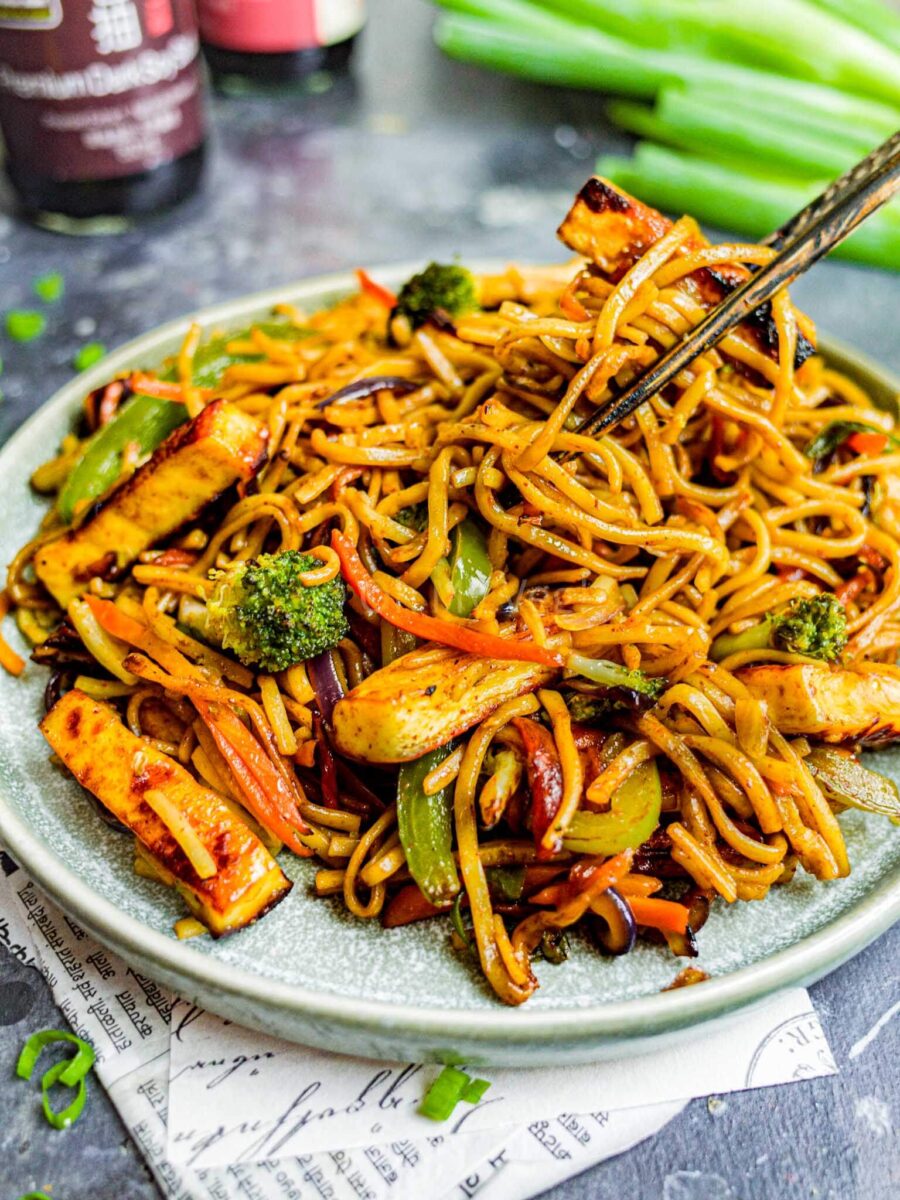 Chopsticks picking up noodles from a plate of paneer hakka noodles.