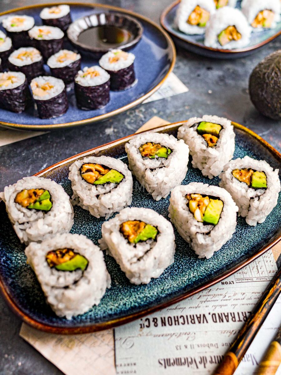 Peanut avocado rolls on blue plates, on a dark table.