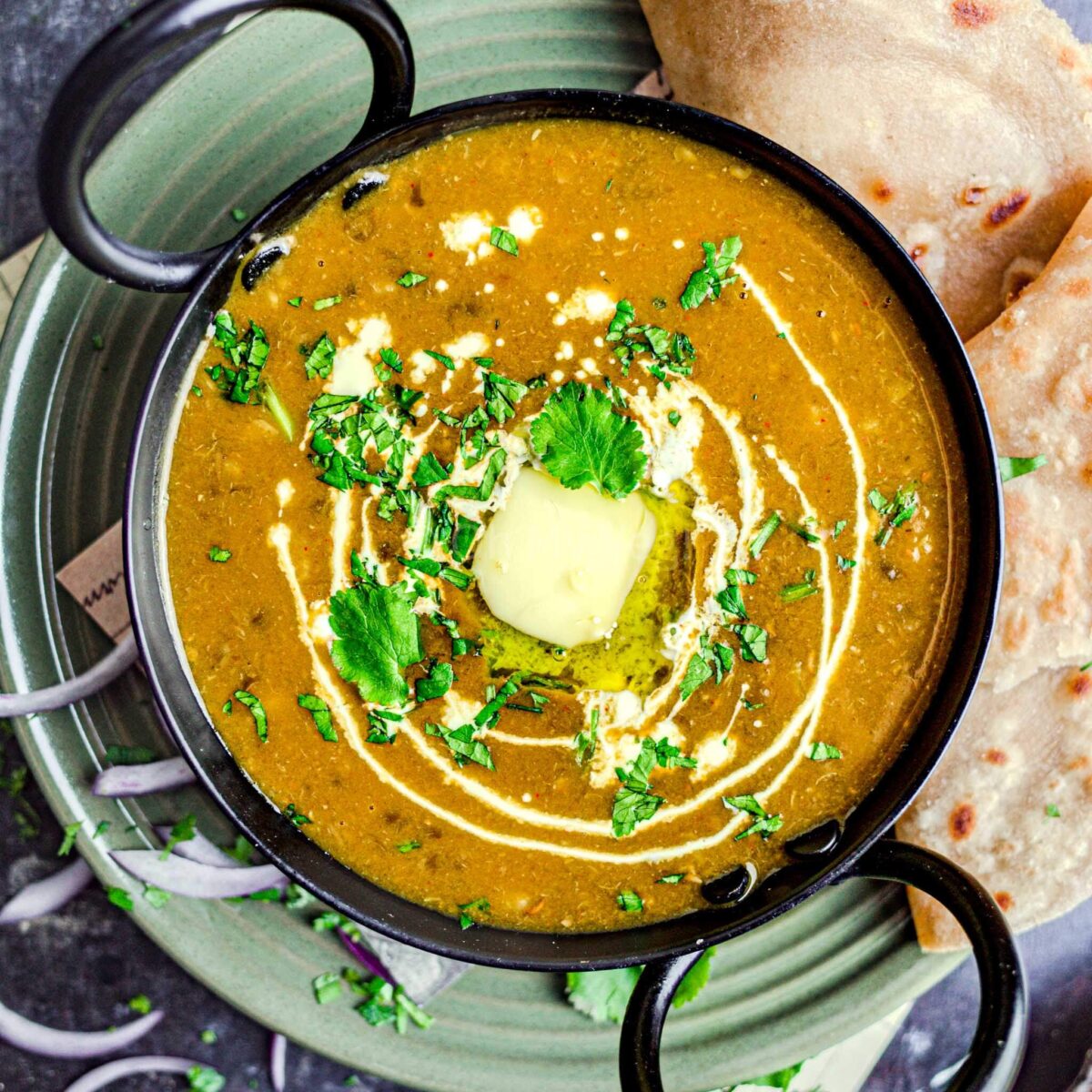 Dal bukhara topped with cream and butter, on a plate with paratha. 