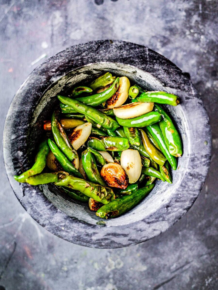 Green chillies and garlic in a black marble mortar and pestle.