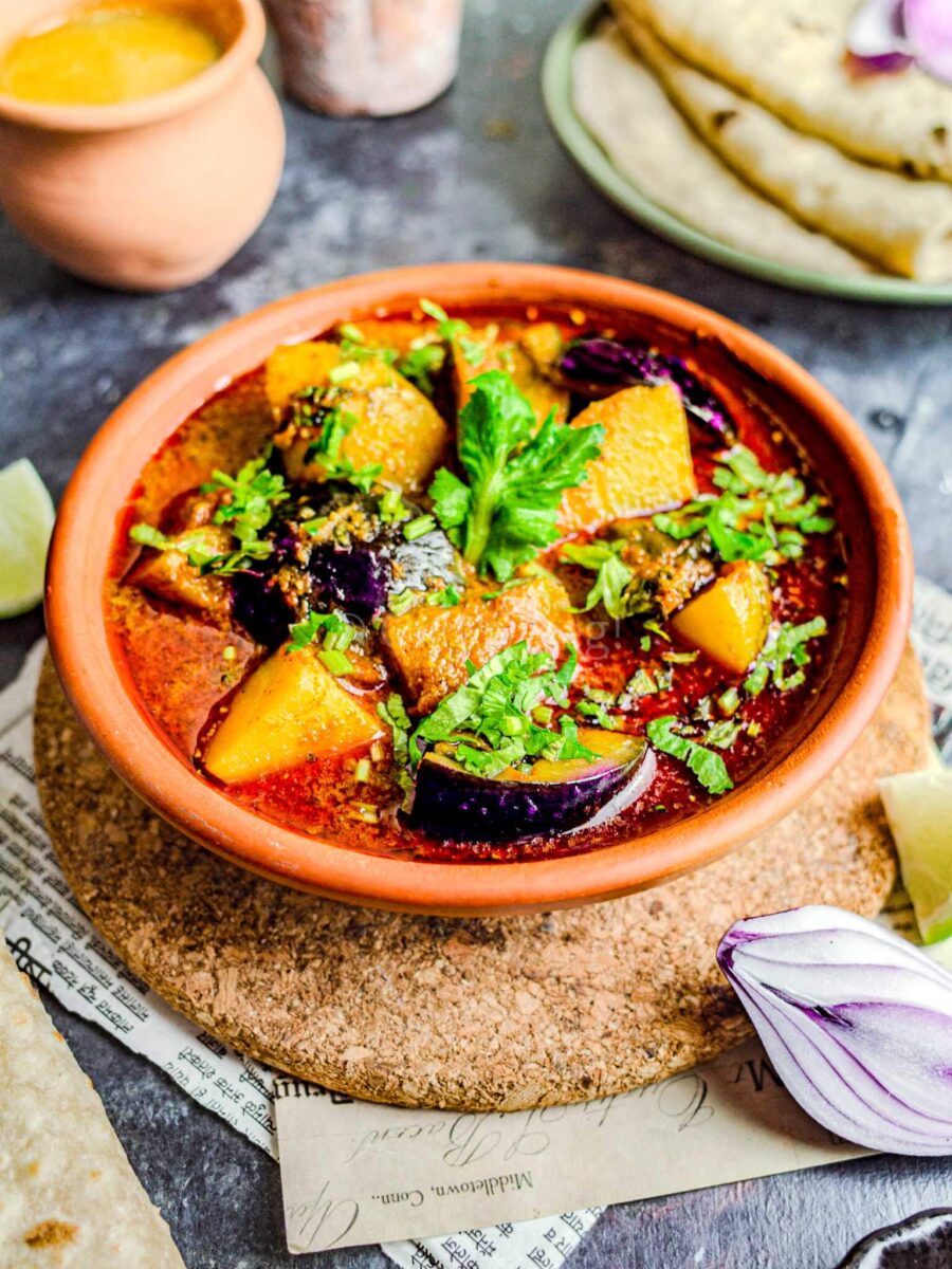 Maharashtrian vangi batata bhaji in a clay bowl, with dal, chapatis, and onion in the background.