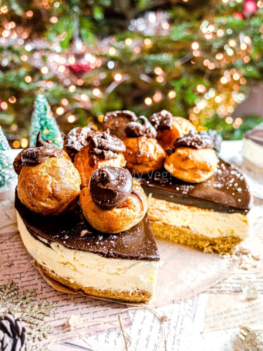 Profiterole cheesecake with a slice cut out, and a Christmas tree in the background.