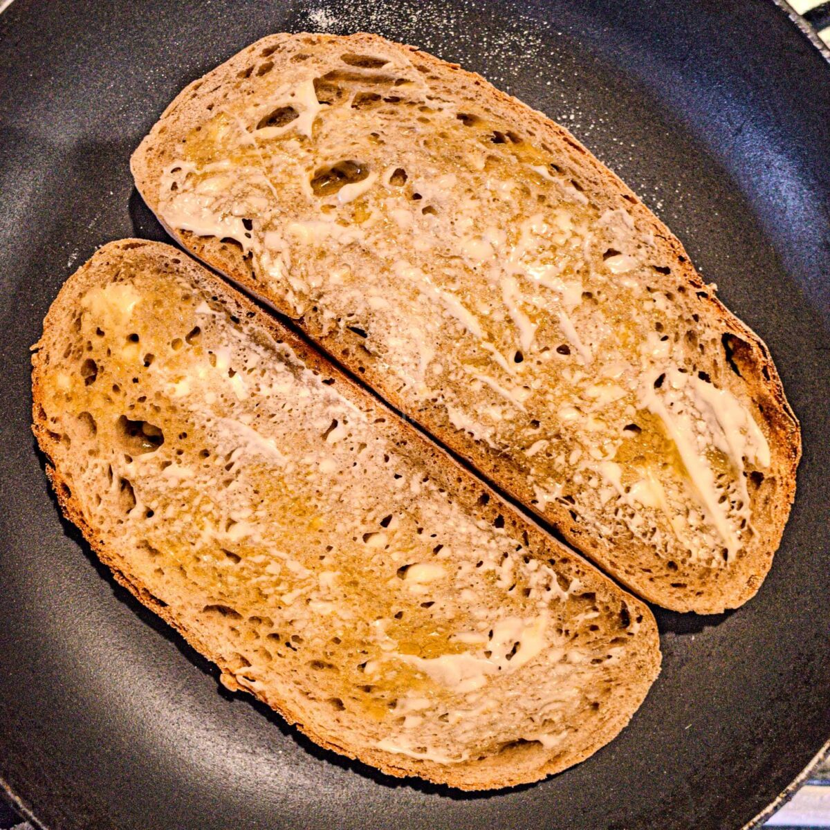 Raw, buttered bread being toasted in a pan.