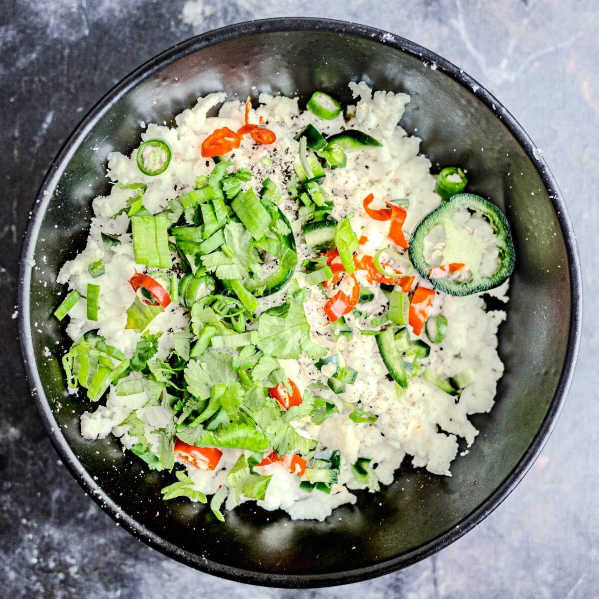 Chillies and coriander added to cheese in a bowl.