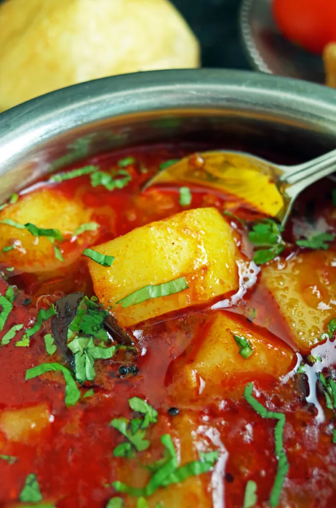 Maharashtrian Batata Rassa / Potato Curry in a steel bowl topped with fresh coriander