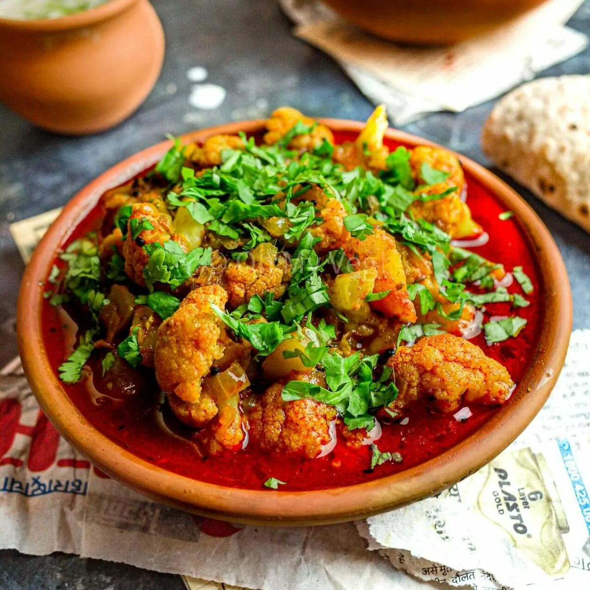 Maharashtrian Flower Batata Rassa in a clay pot, with raita and bhindi masala in the background.