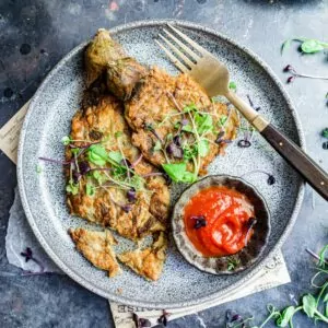 Tortang talong on a plate with banana ketchup and greens.