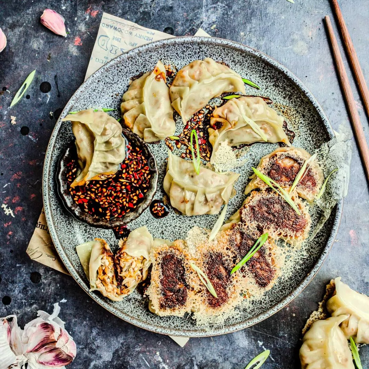 Vegan tofu potstickers with a crispy dumpling skirt on a grey plate with a dipping sauce and chopsticks.