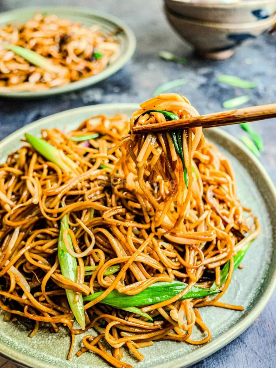 Chopsticks holding up plain chow mein noodles from a plate.