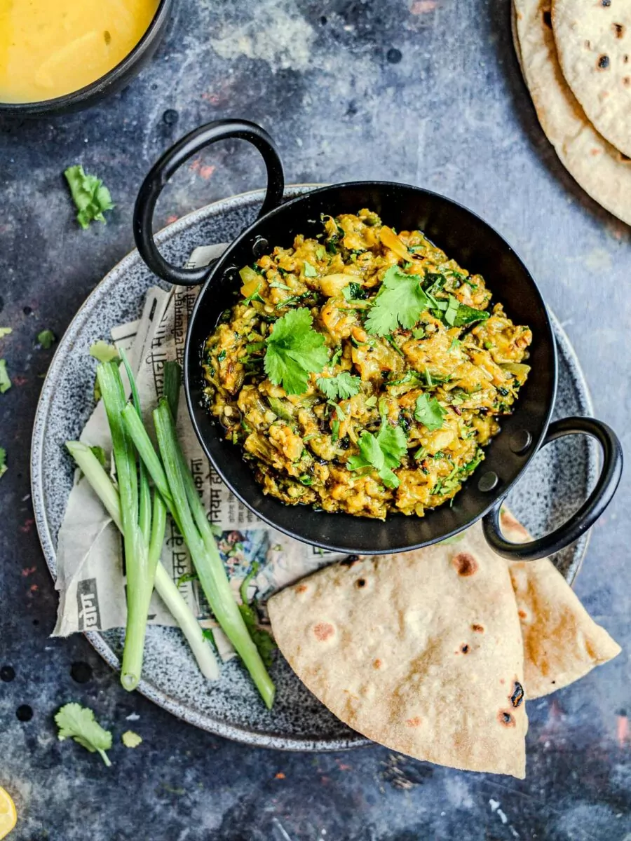 Vangyache bharit in a black kadai with chapati and spring onion on the side.