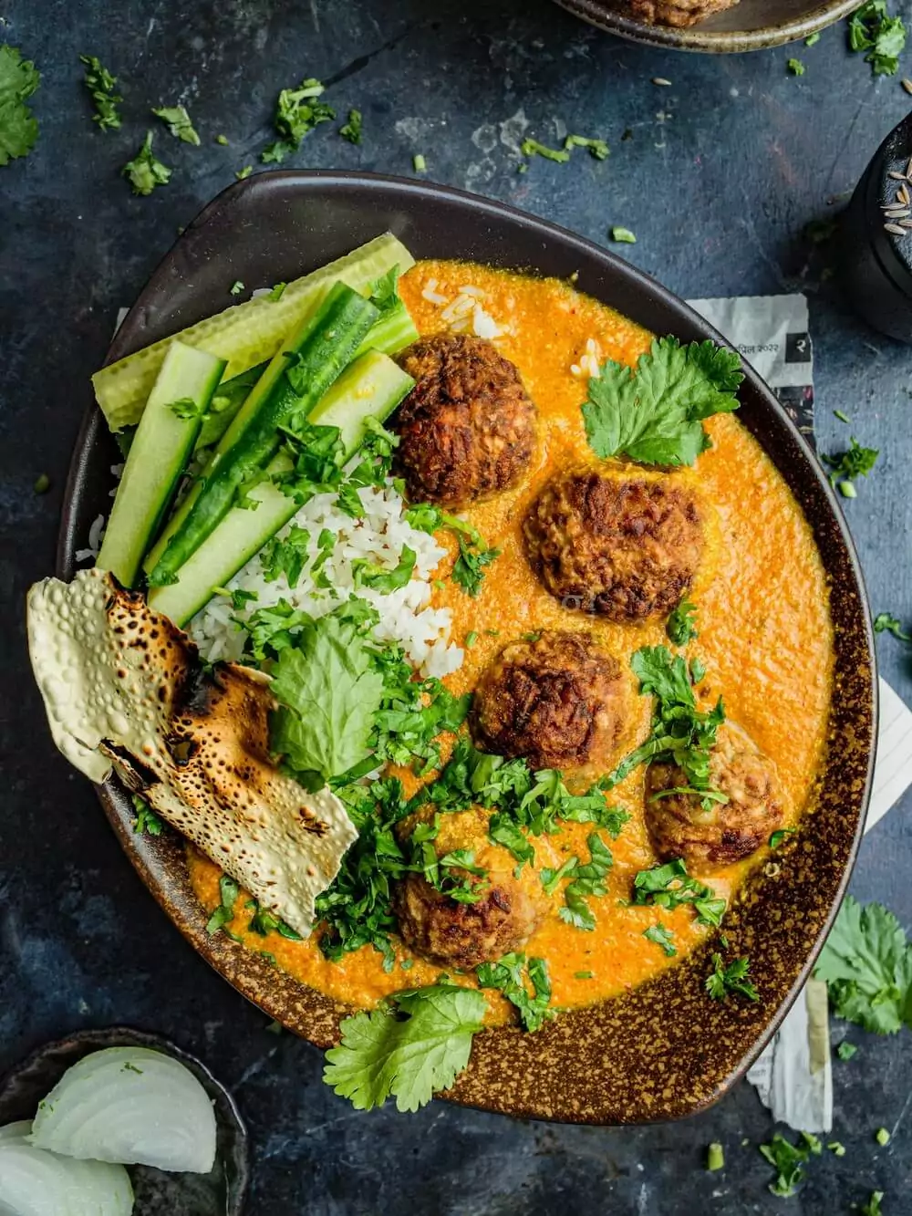 Lauki kofta in a bowl with rice, papad, and cucumber. 