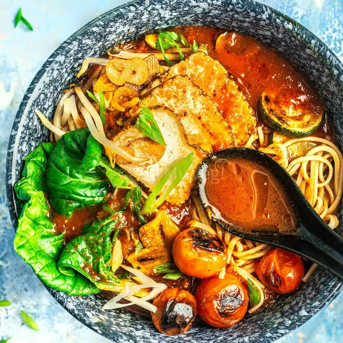 Close up of spicy tomato ramen in a bowl, with a spoon showing the broth.